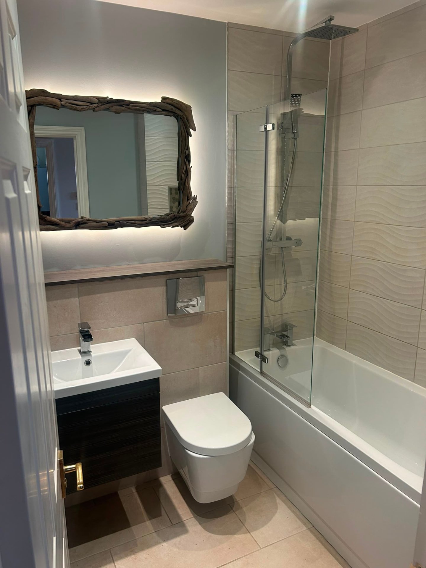 Completed bathroom at Slough with fully tiled bath surround, vanity unit and backlit driftwood mirror